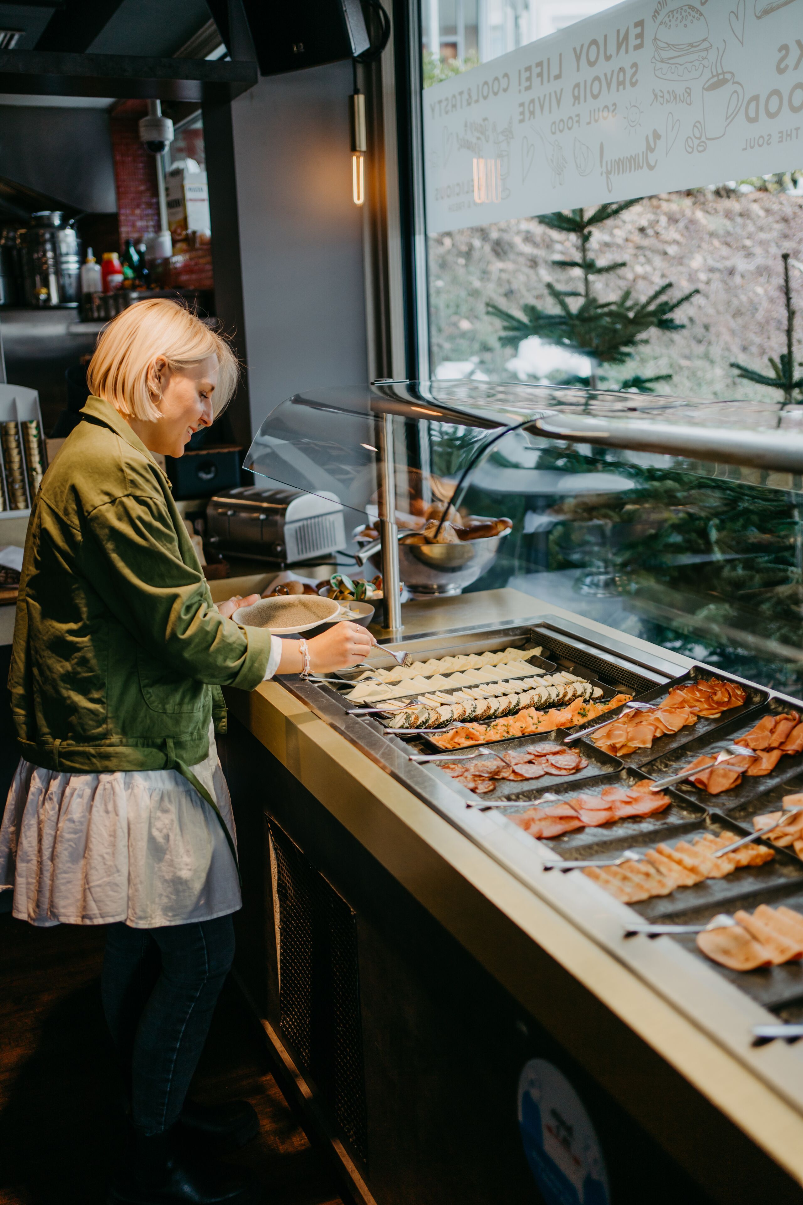 A person serving food at a buffet with various dishes displayed.