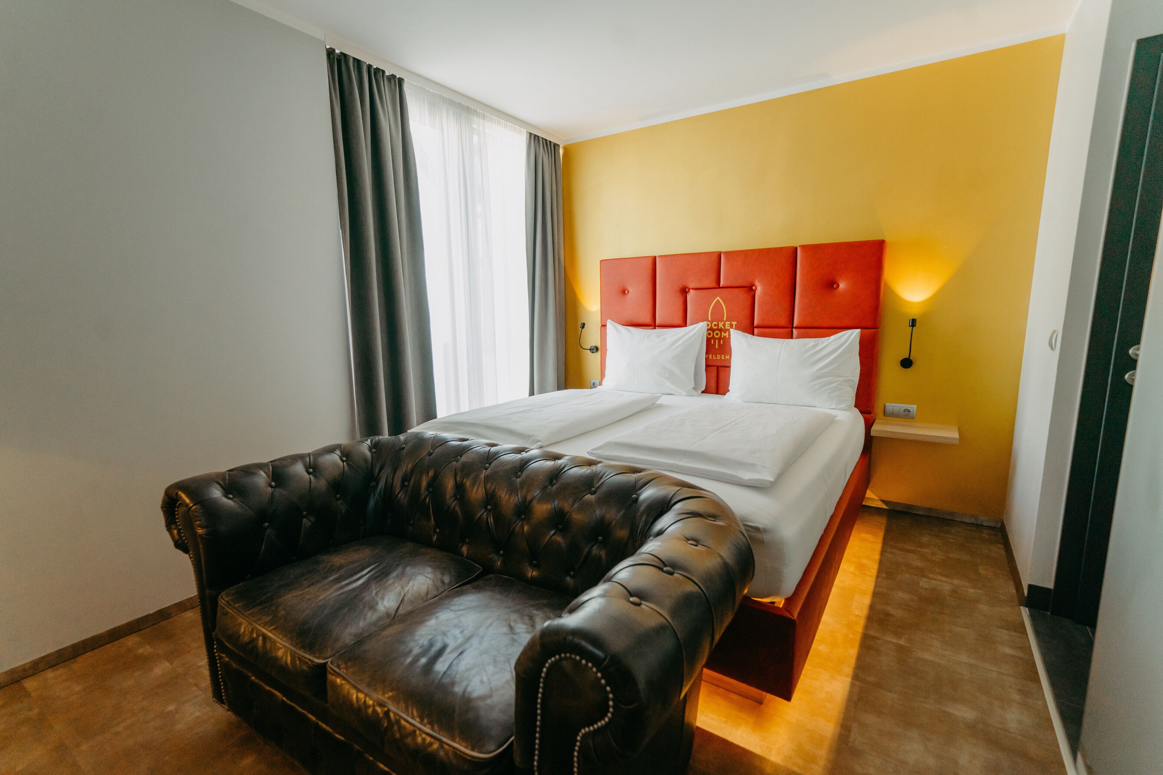 Een hotelkamer met een bed, een leren bank en een felgele muur.