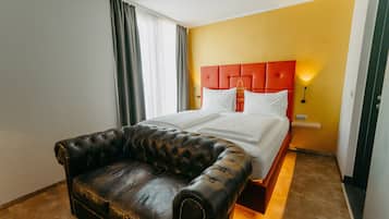 Een hotelkamer met een bed, een leren bank en een felgele muur.