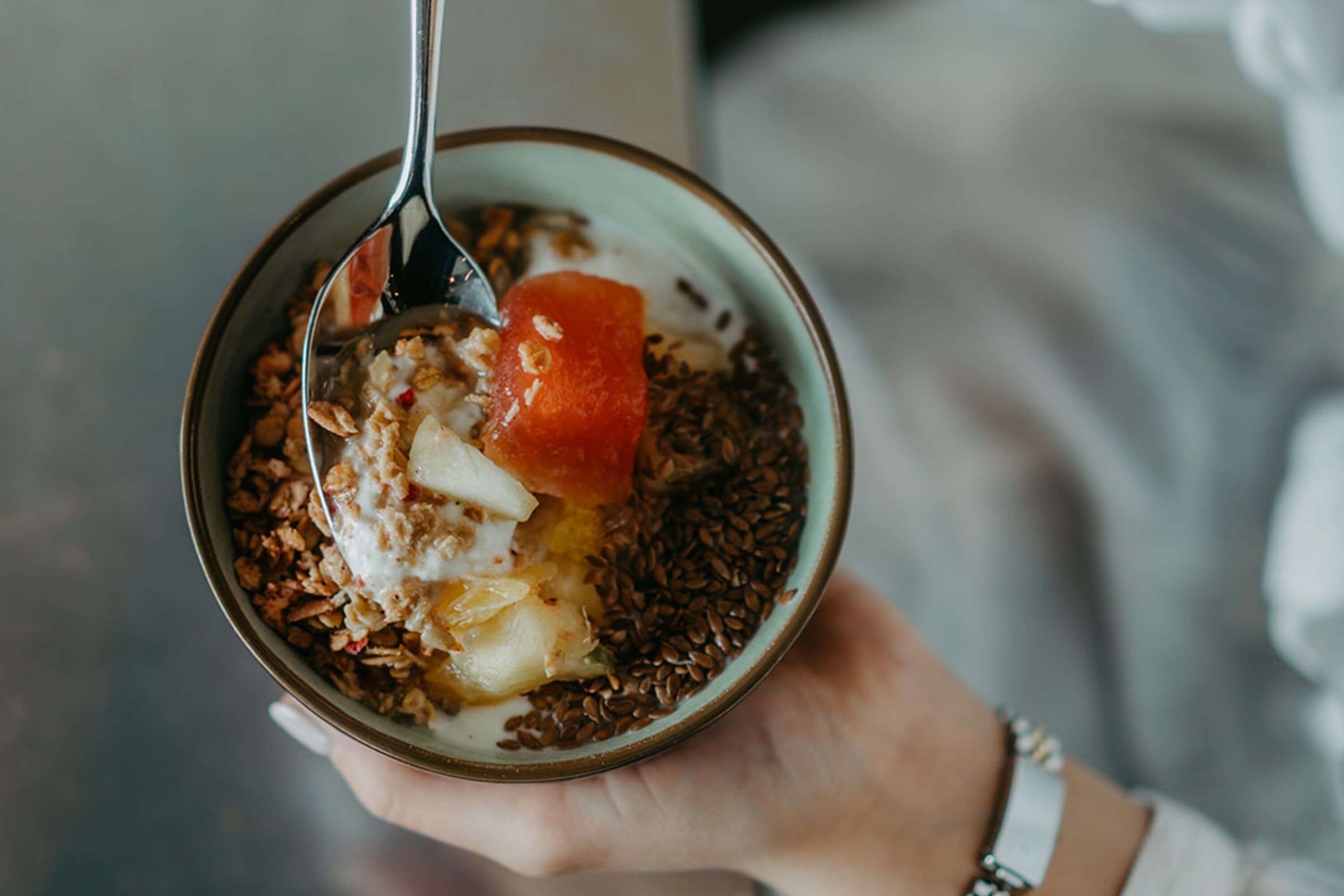 A bowl of cereal with a spoon, held by a person wearing a watch.