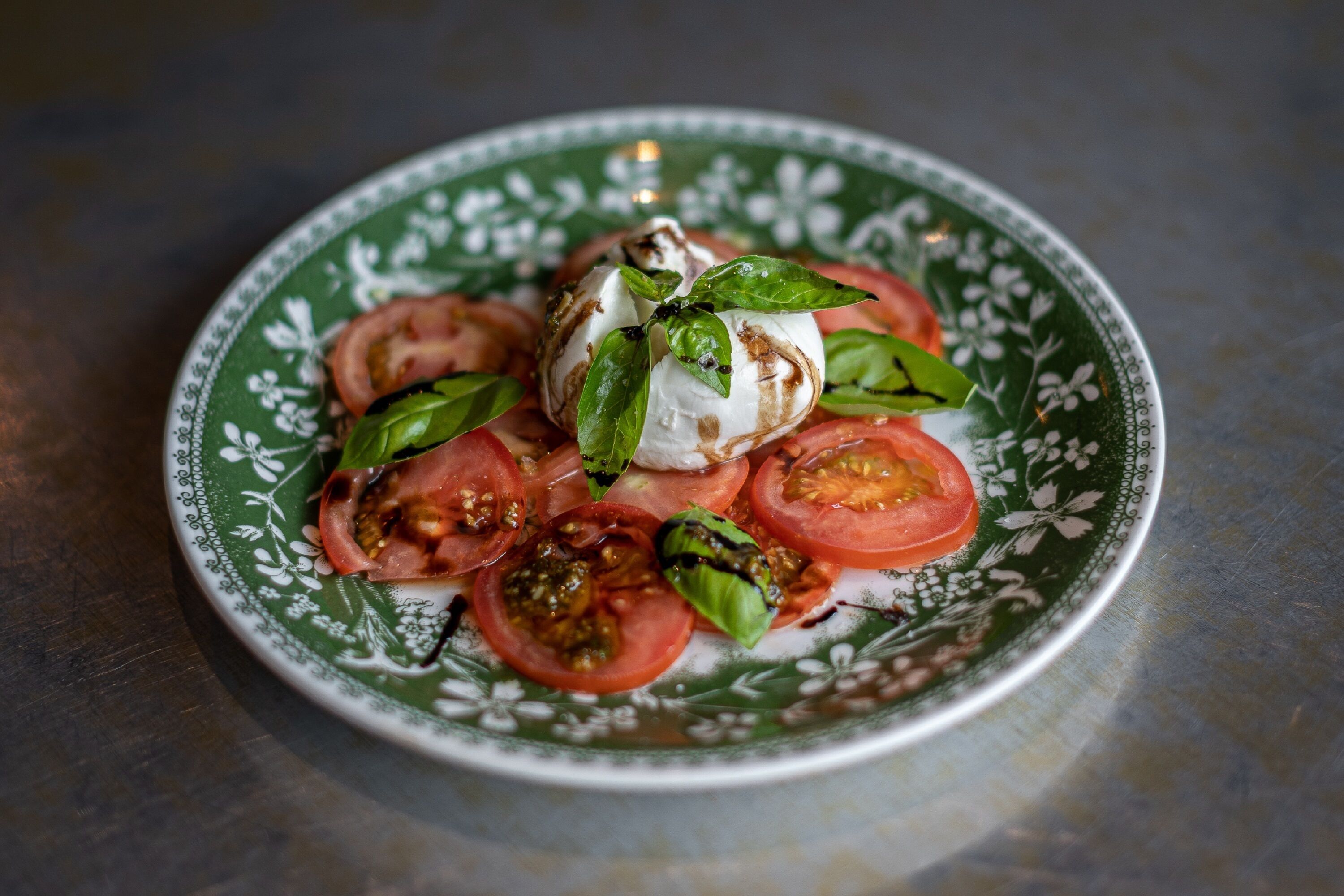 Ensalada caprese en un plato decorativo, con tomates, mozzarella y albahaca.