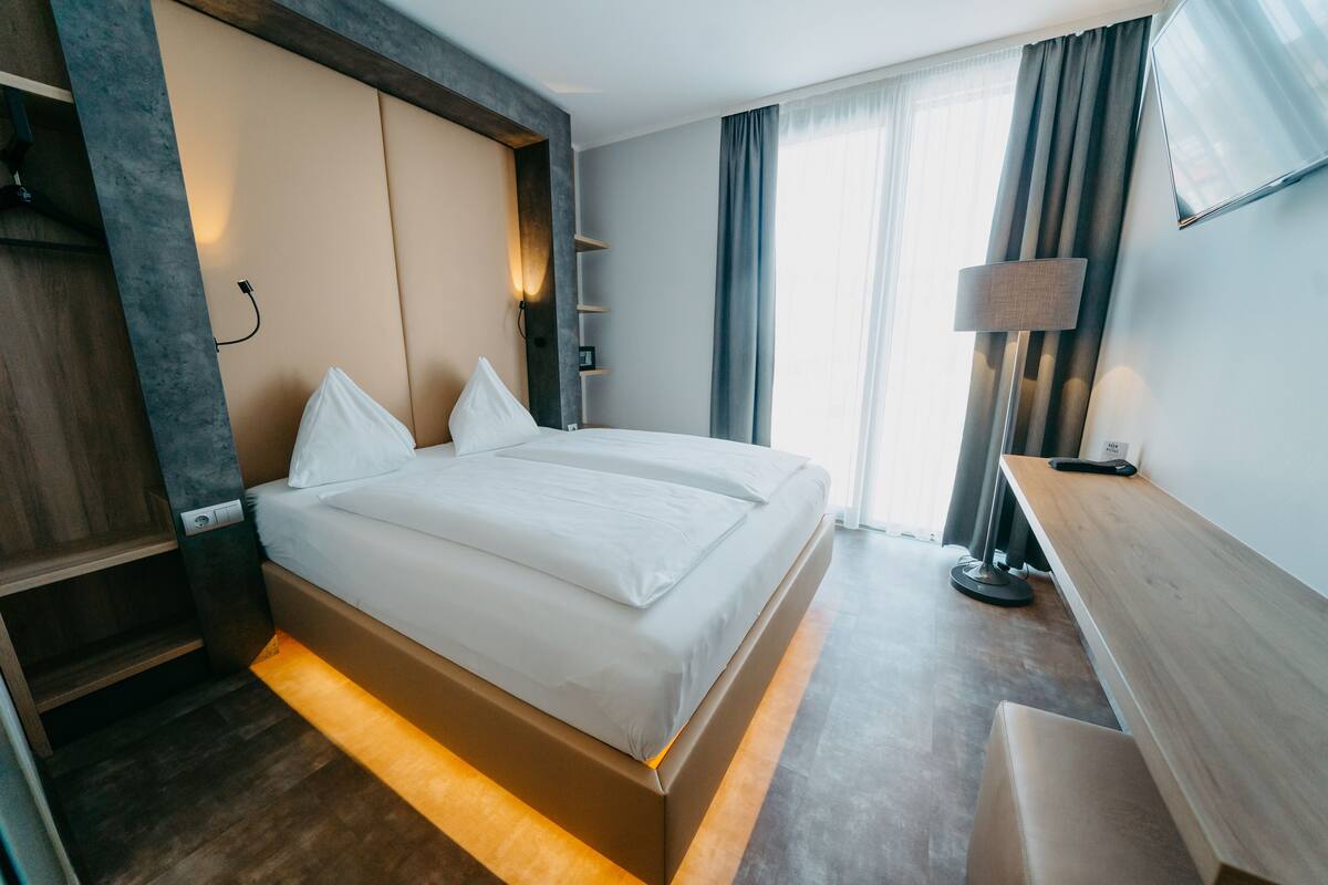 Ett modernt hotellrum med en stor säng, sängbord, ett skrivbord och en tv som är monterad på väggen.