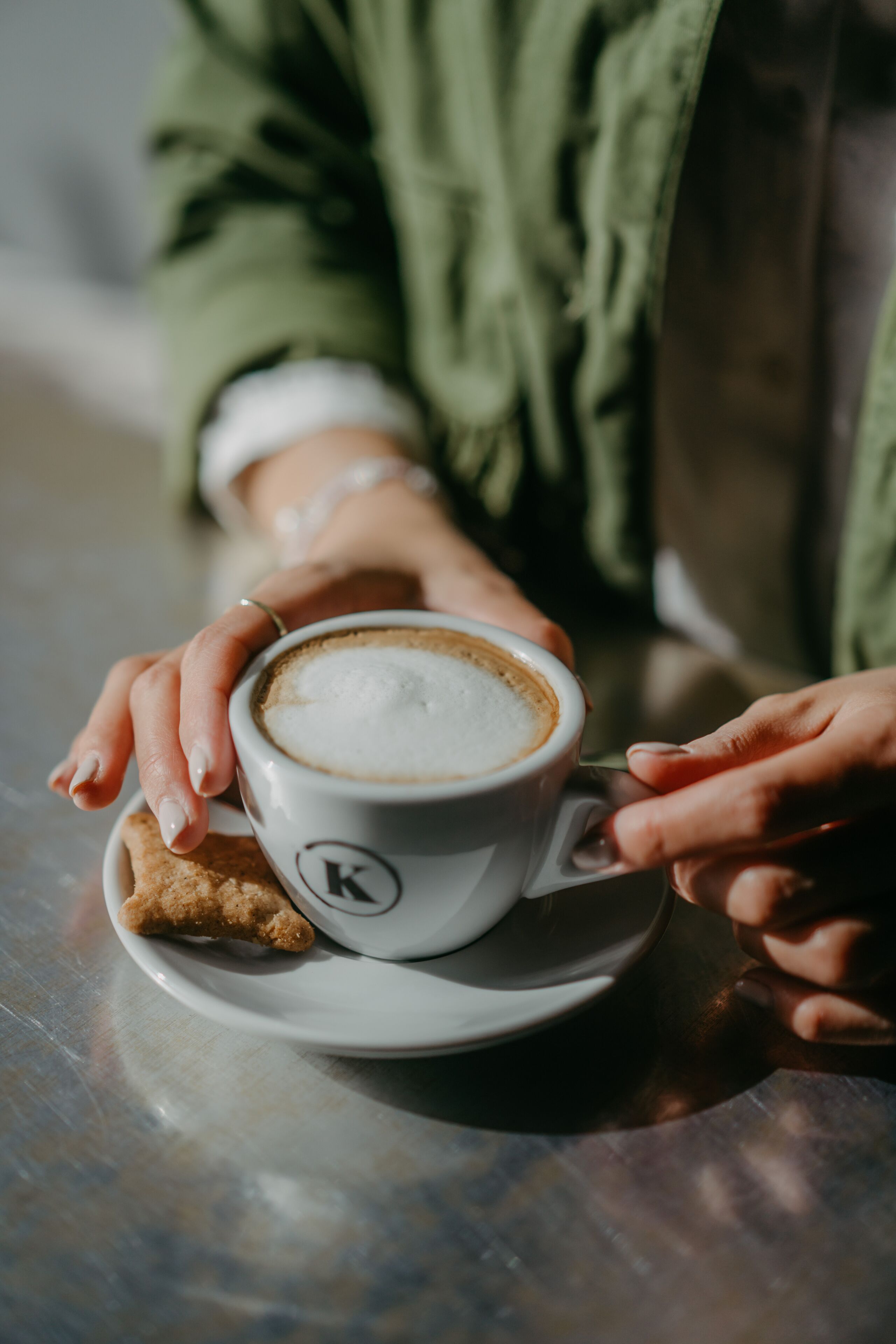 A cup of coffee on a saucer with a logo, held by hands.