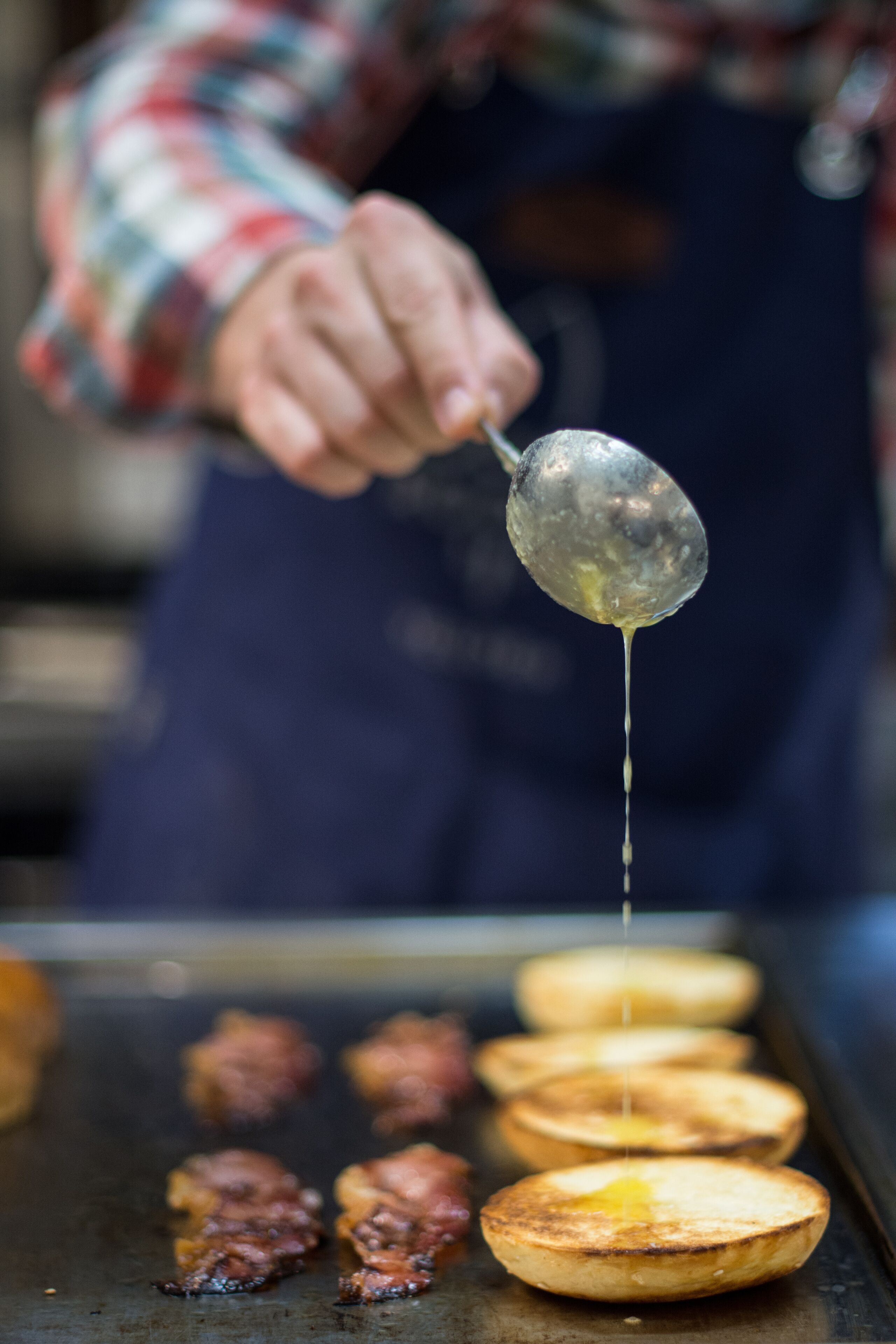 Une personne est en train de préparer des crêpes sur une plaque de cuisson et y verse du sirop.