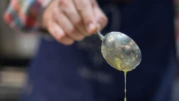 A person cooking pancakes on a griddle with syrup being poured over them.