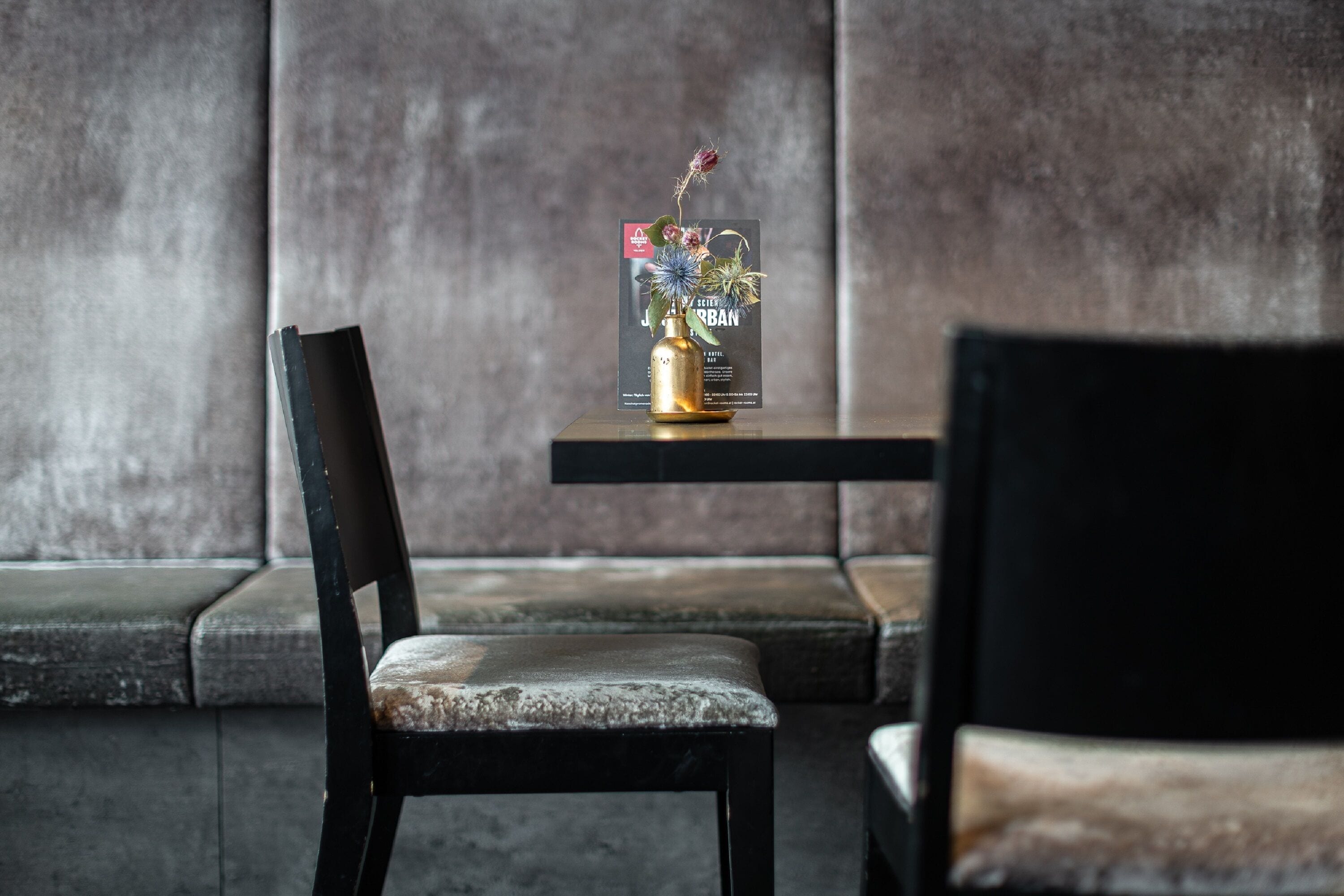 A modern interior with a black cushioned bench, a small table with a magazine, and a dark-colored chair.
