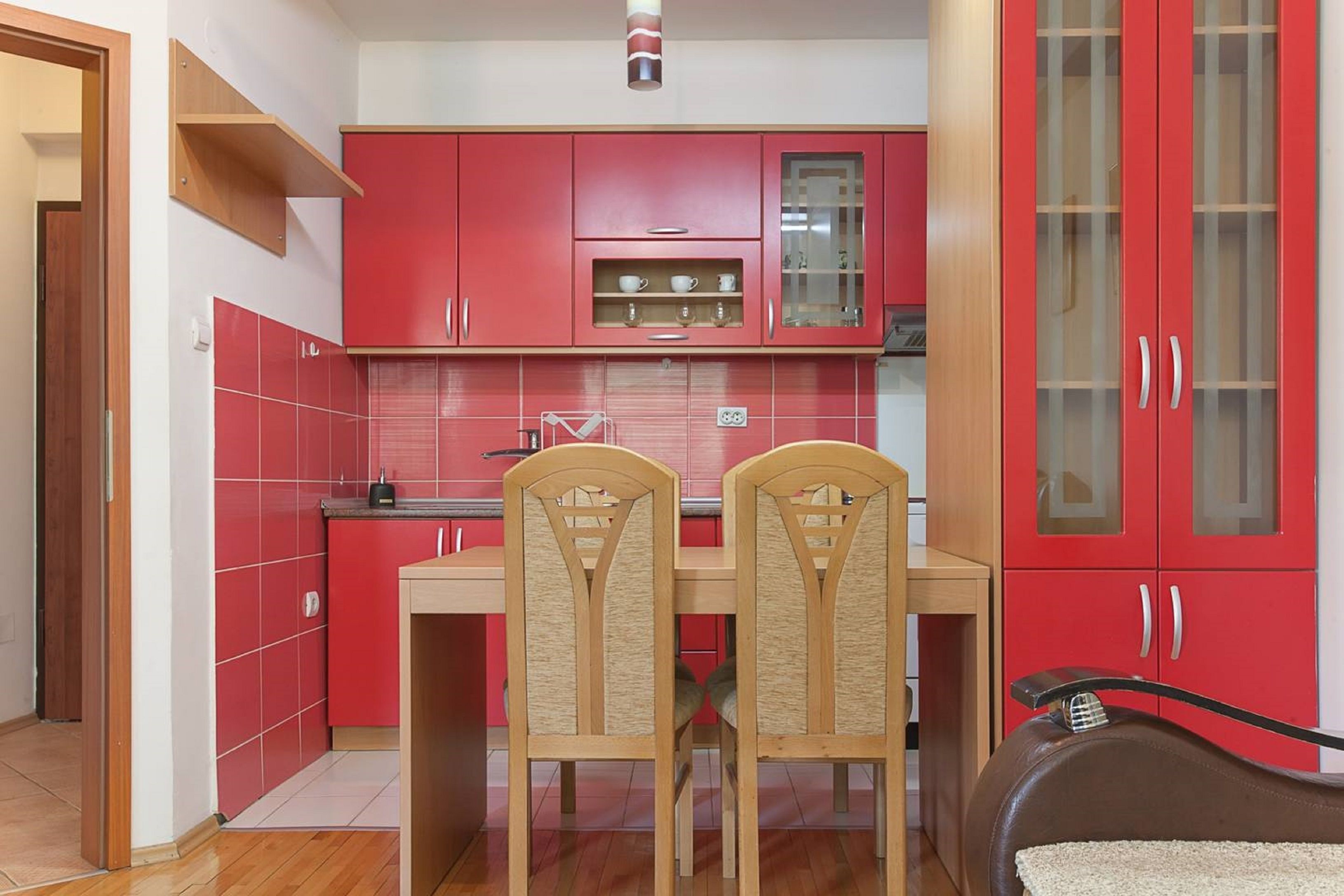 Una cucina compatta con mobili rossi, un tavolo da pranzo in legno e due sedie.