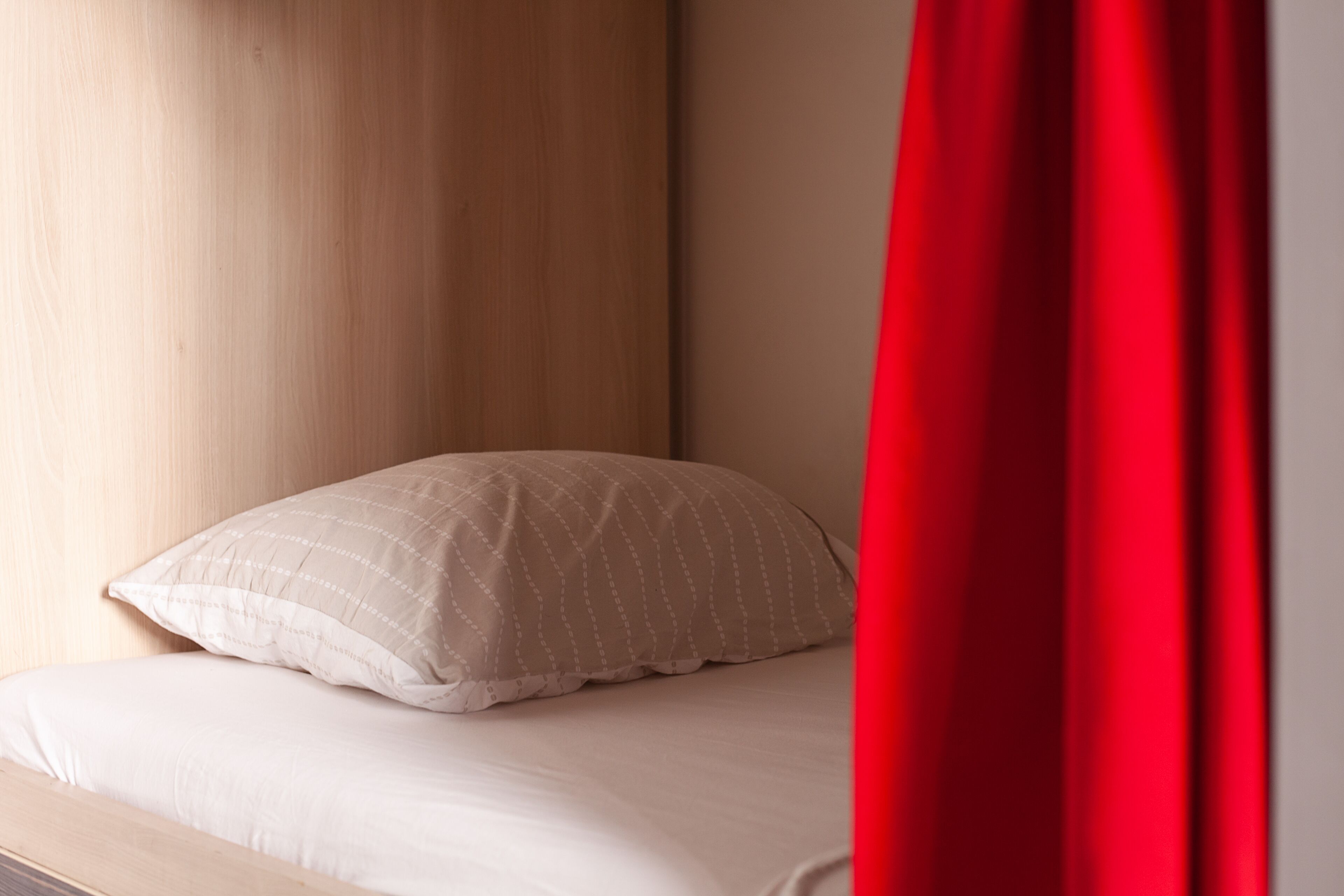 Een bed met een beige kussen en een rood gordijn dat gedeeltelijk is opengetrokken.