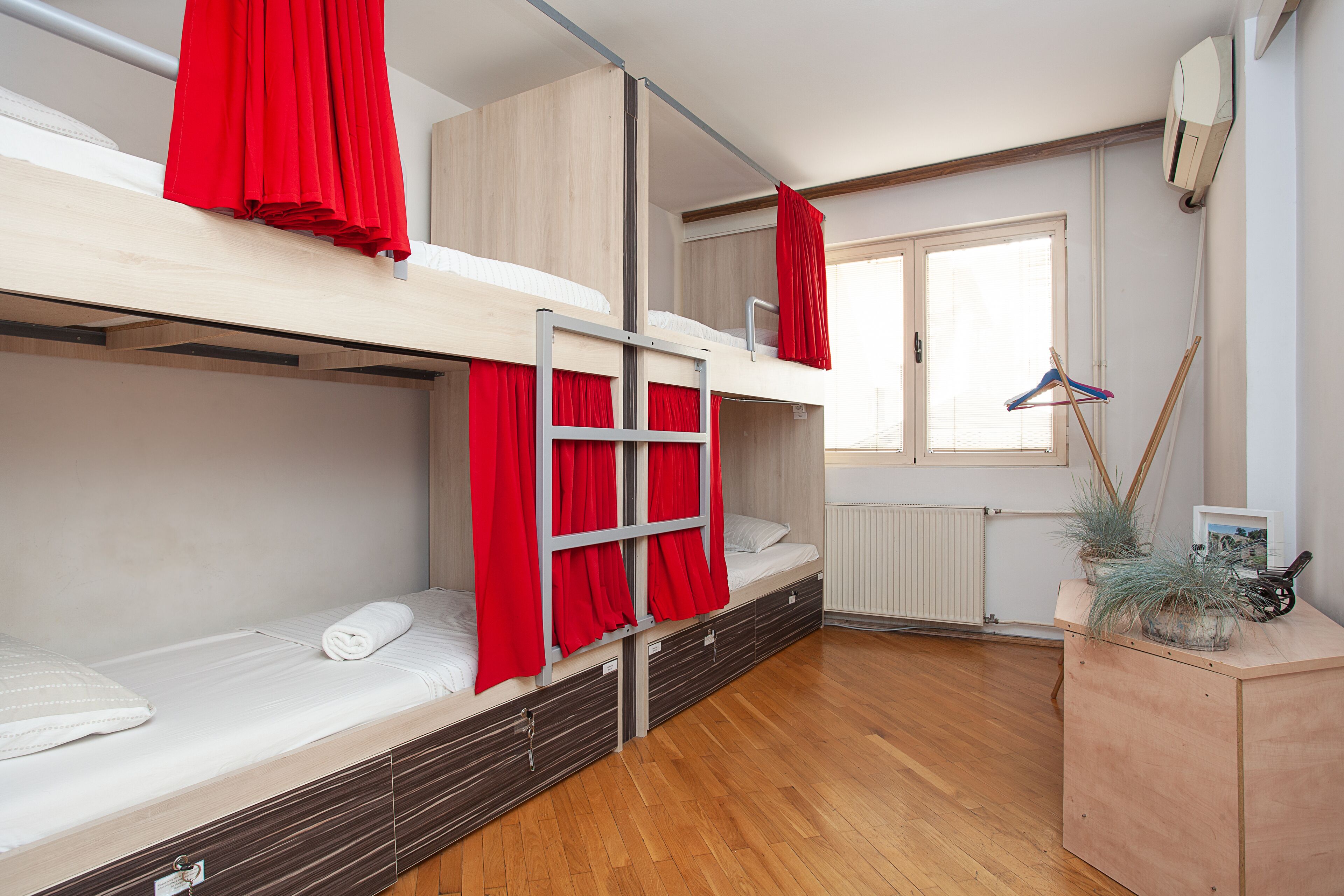 Ein Schlafsaalzimmer mit Etagenbetten, Holzboden, Heizkörper und einem kleinen Holzschrank mit Pflanzen.