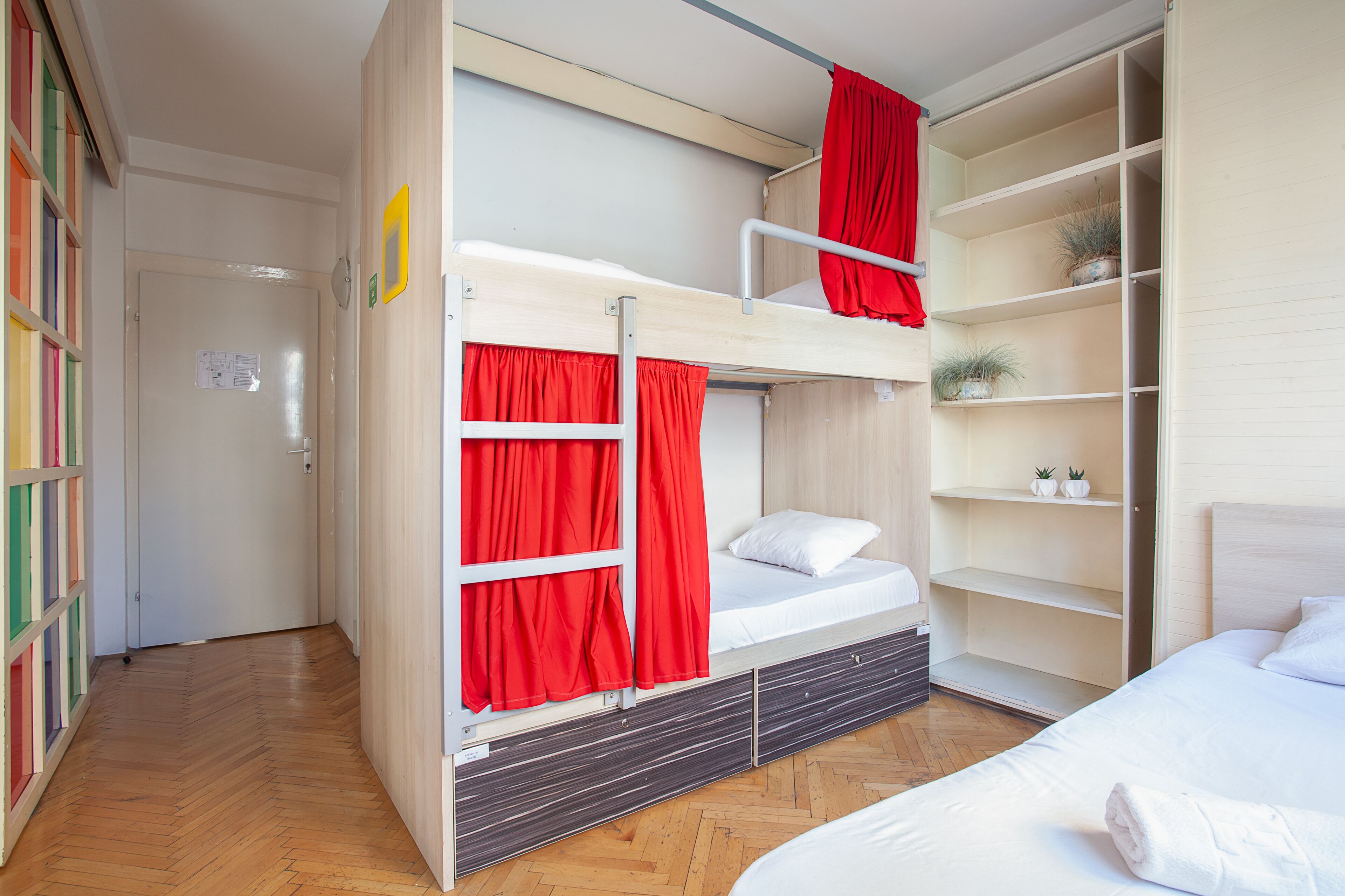 A bunk bed room with red curtains, a wooden floor, and a white bed.
