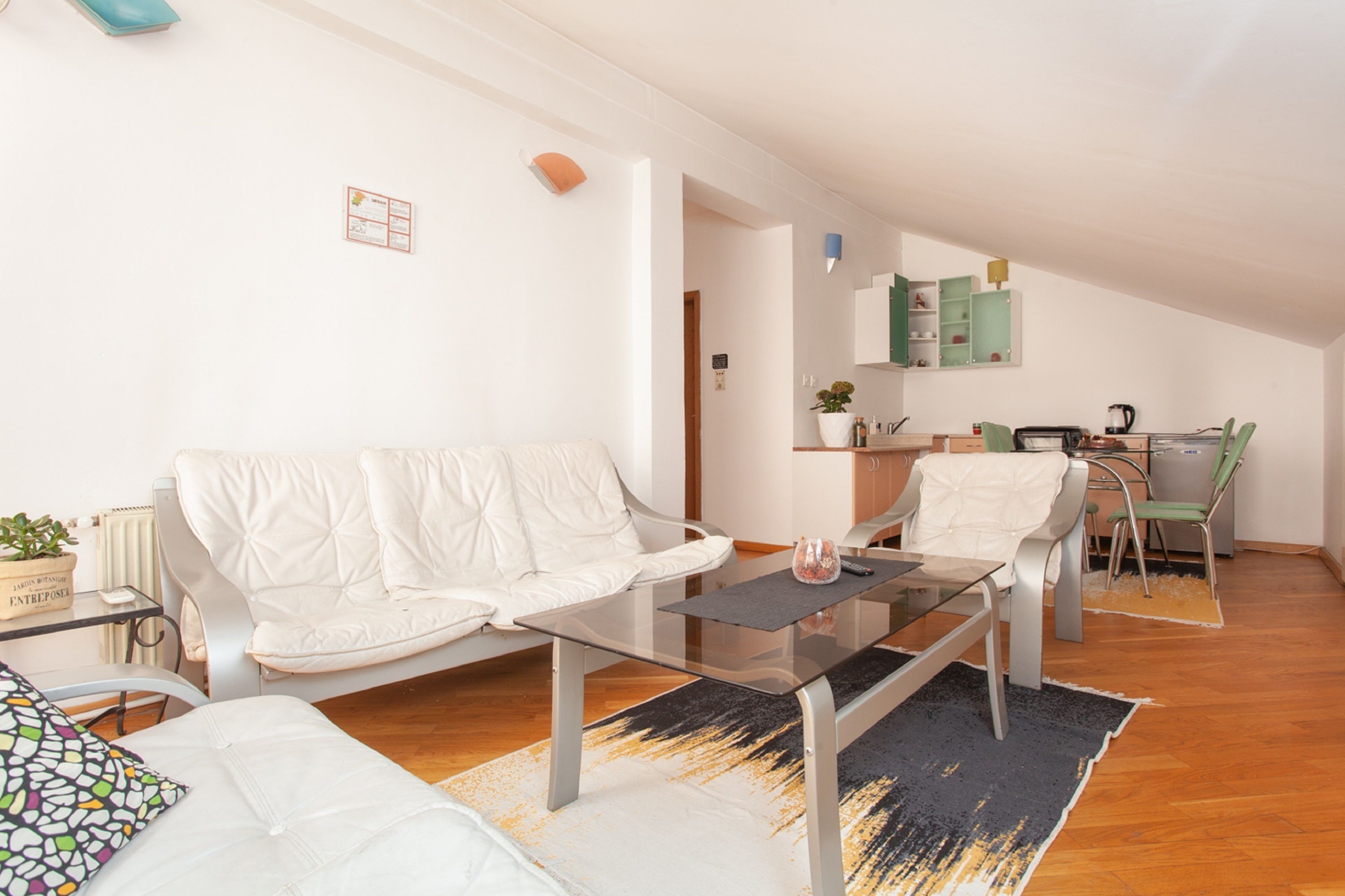 A modern living room with a white sofa, a glass coffee table, and a dining area with a green chair.