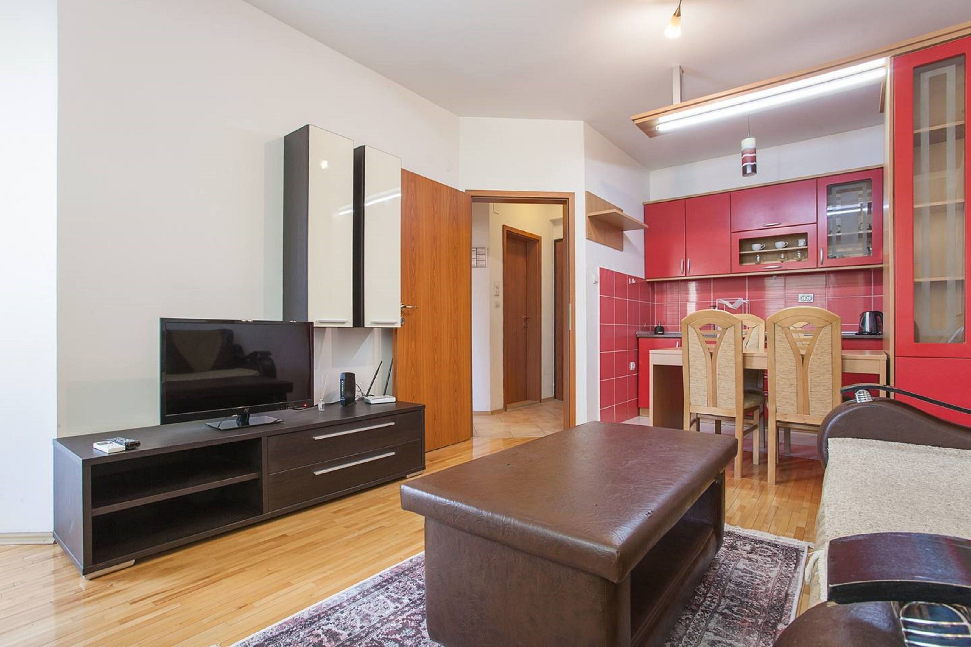 A compact living space with a TV, entertainment unit, and a kitchenette with red cabinets.
