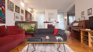 A living room with a red sofa, a black sofa with red cushions, a wooden coffee table, a fish tank, and a piano. - Urban Hostel & Apartments (Skopje)