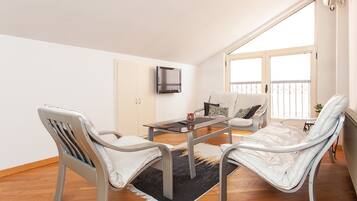 A modern living room with two white chairs, a glass coffee table, and a flat-screen TV mounted on the wall.