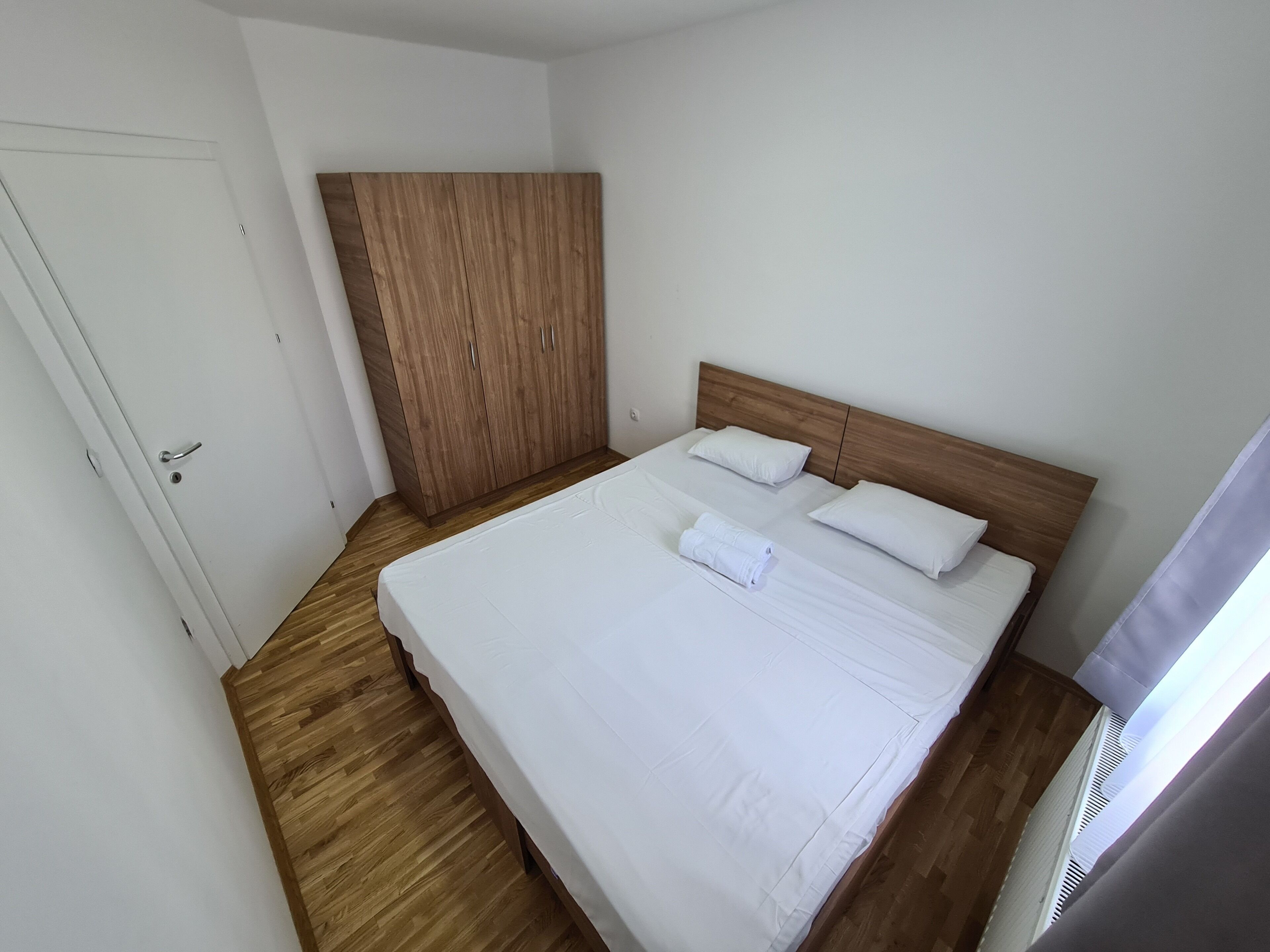 Un lit bien fait, avec du linge de lit blanc et des oreillers, une armoire en bois et une porte blanche.