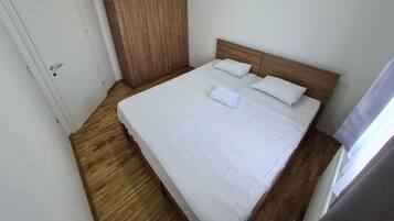 Ein ordentlich bezogenes Bett mit weißen Leinen und Kissen, ein Holzschrank und eine weiße Tür.
