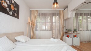 A modern hotel room with a large bed, a bedside table, a mirror, and a window with sheer curtains. - Urban Hostel & Apartments (Skopje)