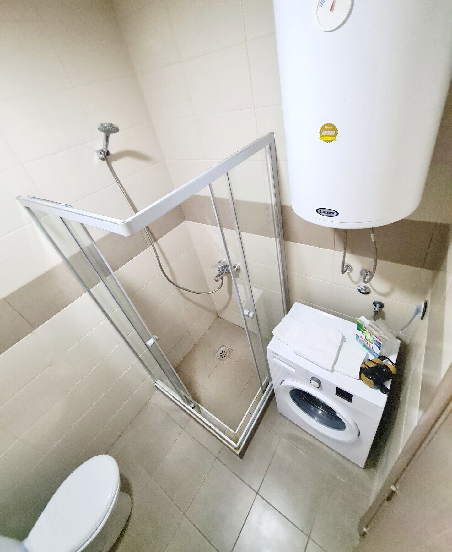 A bathroom with a glass shower enclosure, a toilet, and a washing machine.