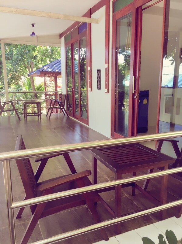 A covered outdoor seating area with wooden tables and chairs, a glass railing, and a view of greenery outside. - Reggae Village (Ko Pha-ngan)