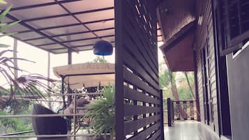 Un espacio al aire libre techado con una mesa y sillas, rodeado de plantas.