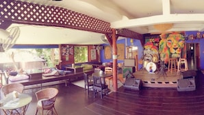 A spacious indoor area with multiple seating arrangements, including sofas and chairs, and a stage with musical instruments. - Reggae Village (Ko Pha-ngan)