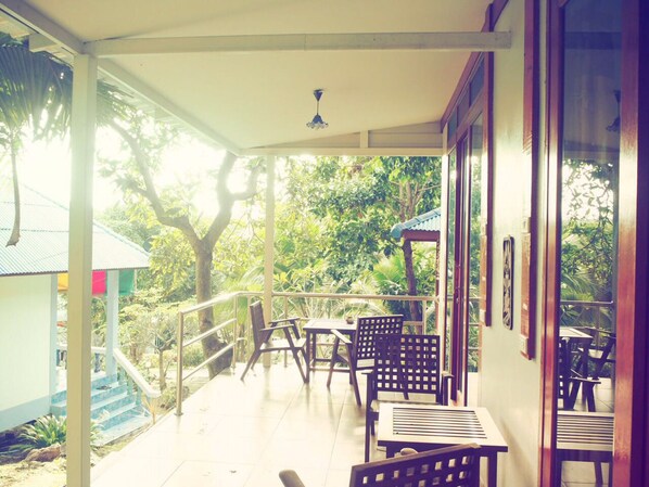 A covered outdoor area with tables and chairs, a staircase leading to a building, and a view of greenery. - Reggae Village (Ko Pha-ngan)