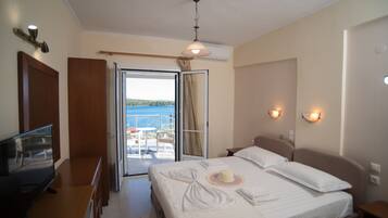A hotel room with a bed, a TV, a desk, and a balcony with a view of the sea.