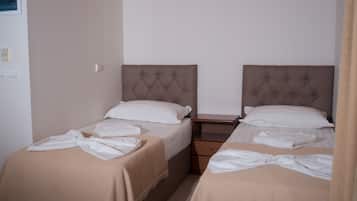 Habitación de hotel con dos camas, cada una con cabecero marrón y ropa de cama blanca. Hay una mesita de noche de madera entre las camas y una pequeña mesa con una lámpara.