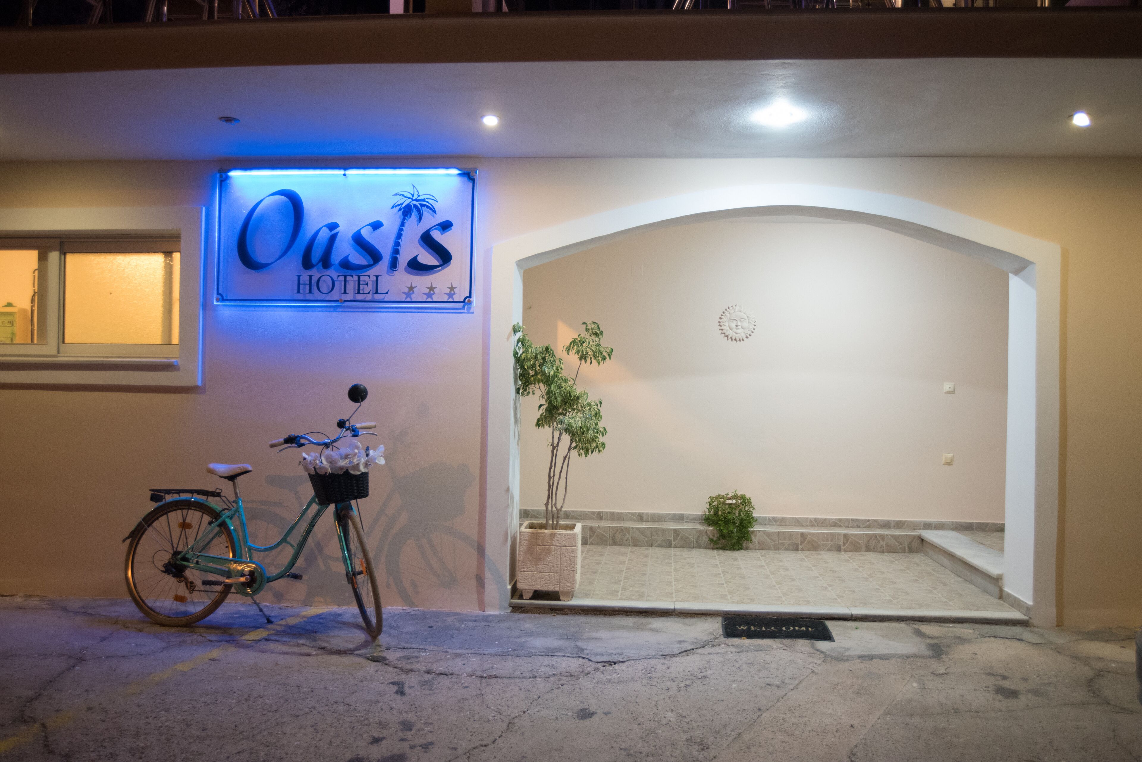 A hotel entrance with a neon sign, a bicycle, and a potted plant.