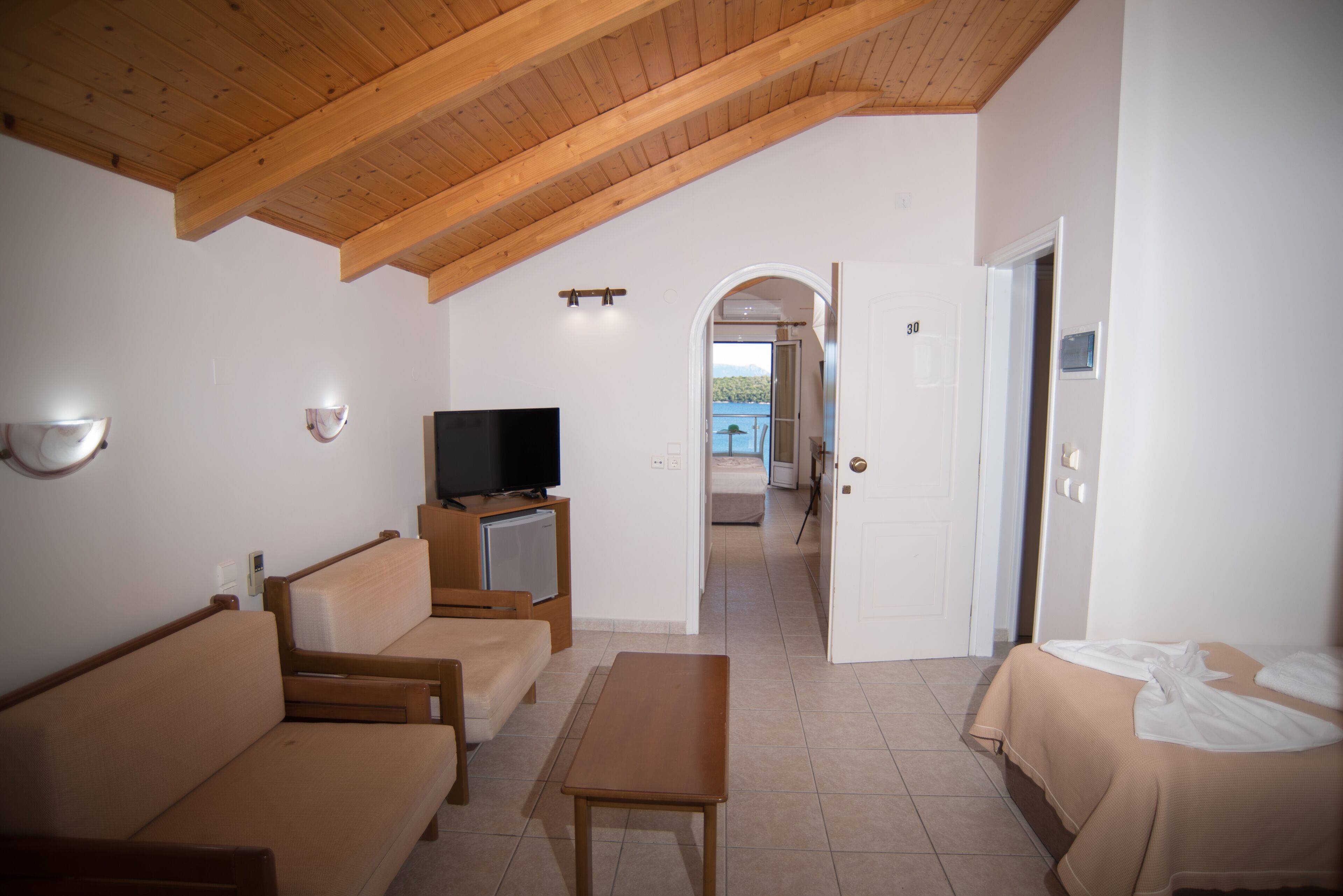Una habitación con techo de madera, un televisor sobre un mueble bajo, un sofá, una mesa y una cama.
