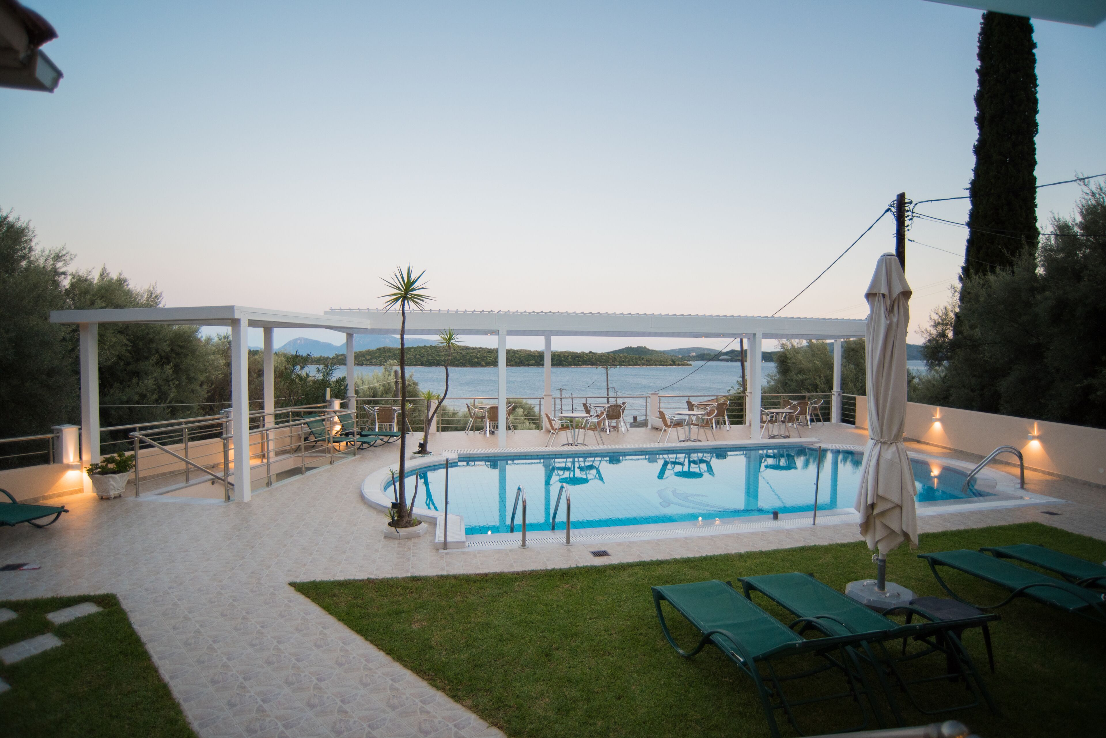 An outdoor swimming pool with a view of the sea, surrounded by lounge chairs and a covered area.