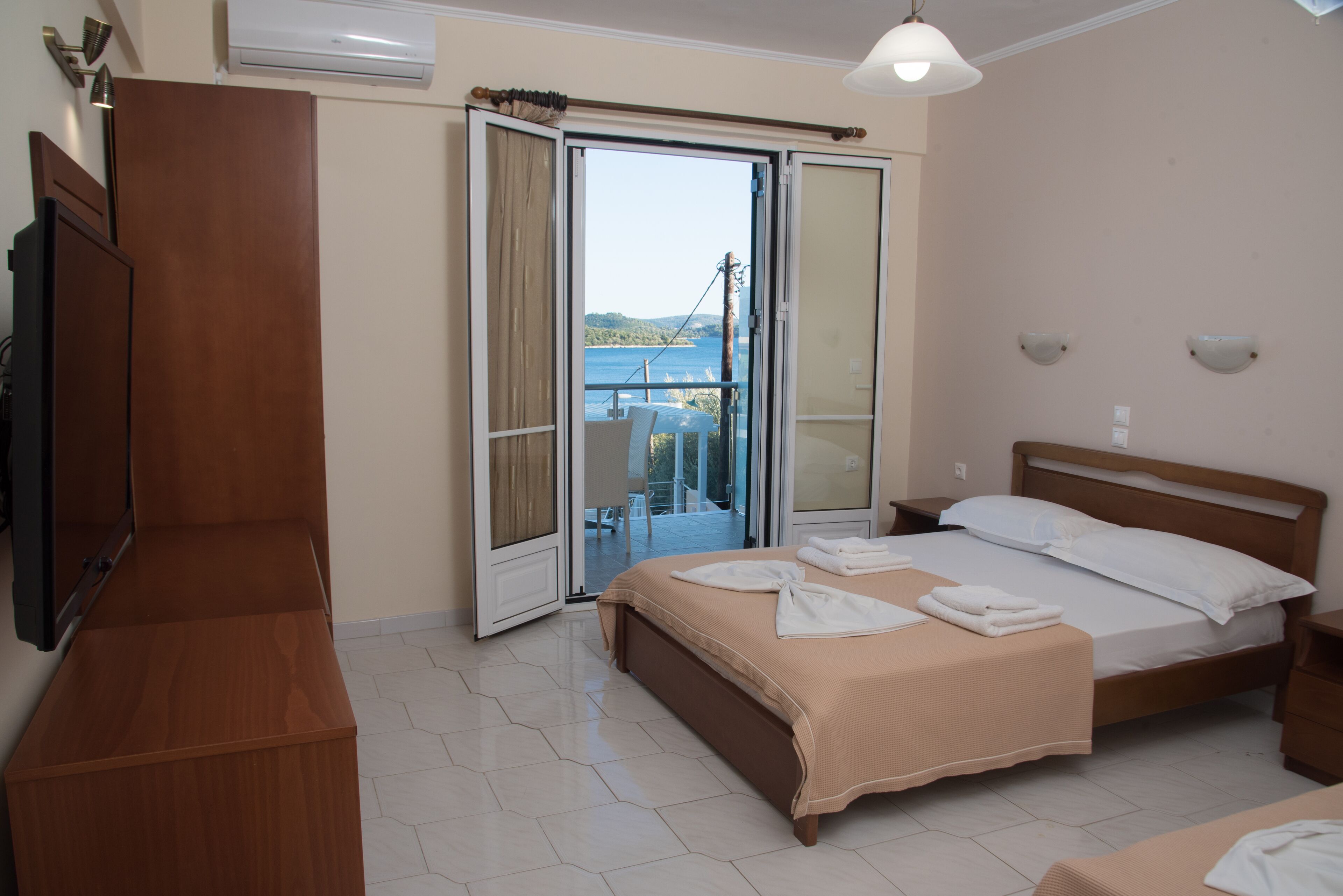 A hotel room with a bed, a TV, a wardrobe, and a balcony with a view of the sea.