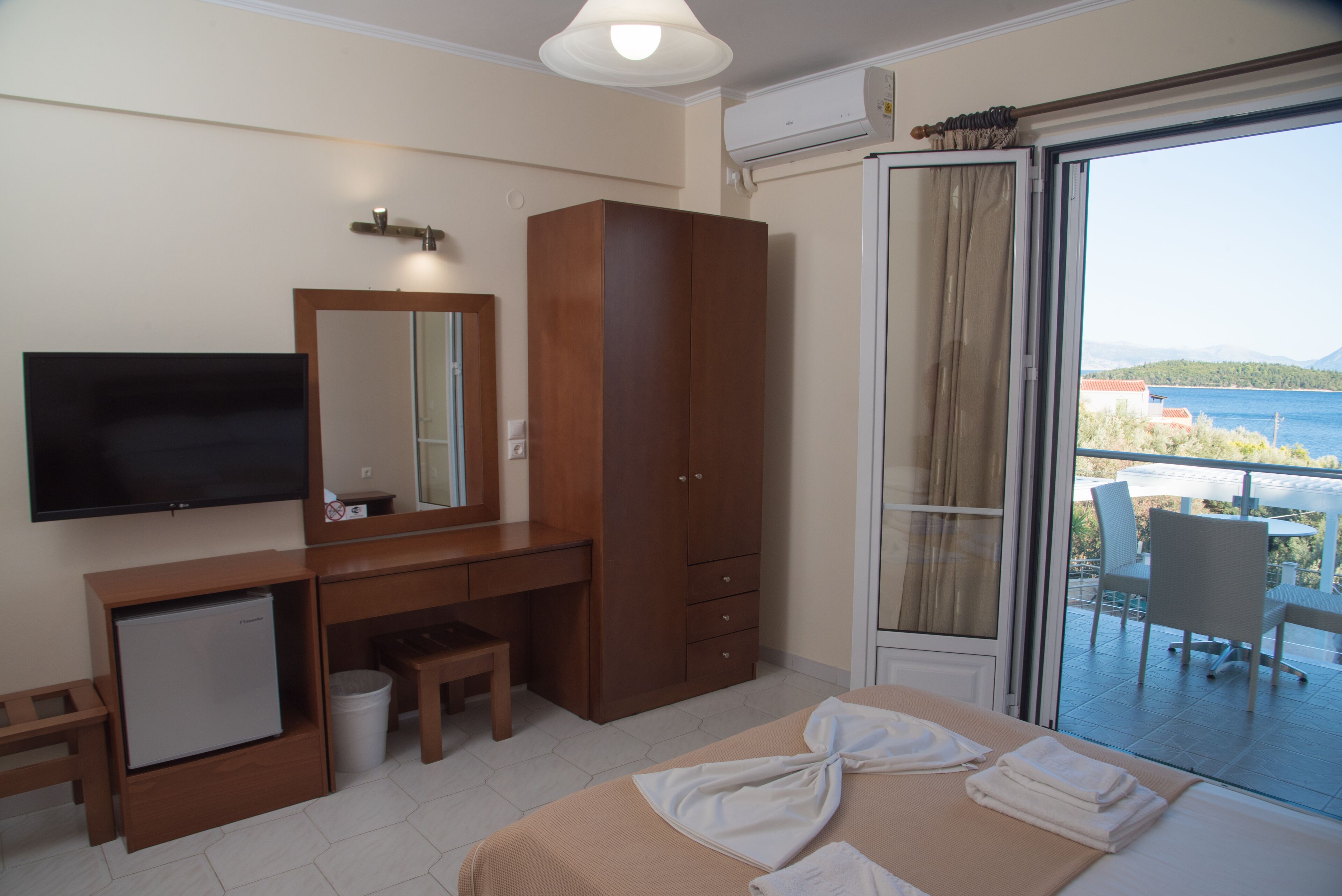 Une chambre d’hôtel comprenant un lit, un bureau, une télévision, une armoire, un balcon avec vue sur la mer et une chaise.