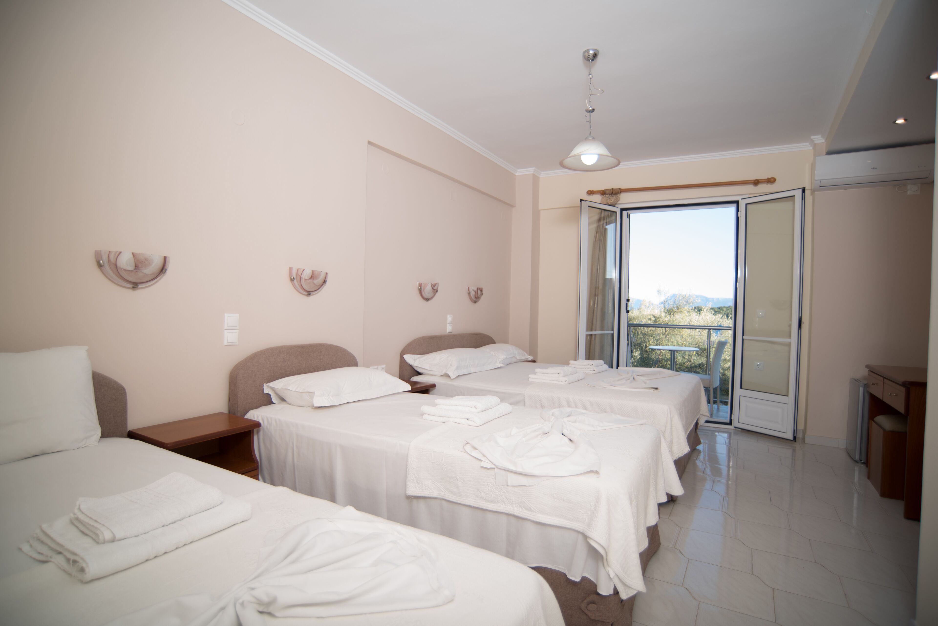 A hotel room with three beds, a balcony, and a view of the outdoors.