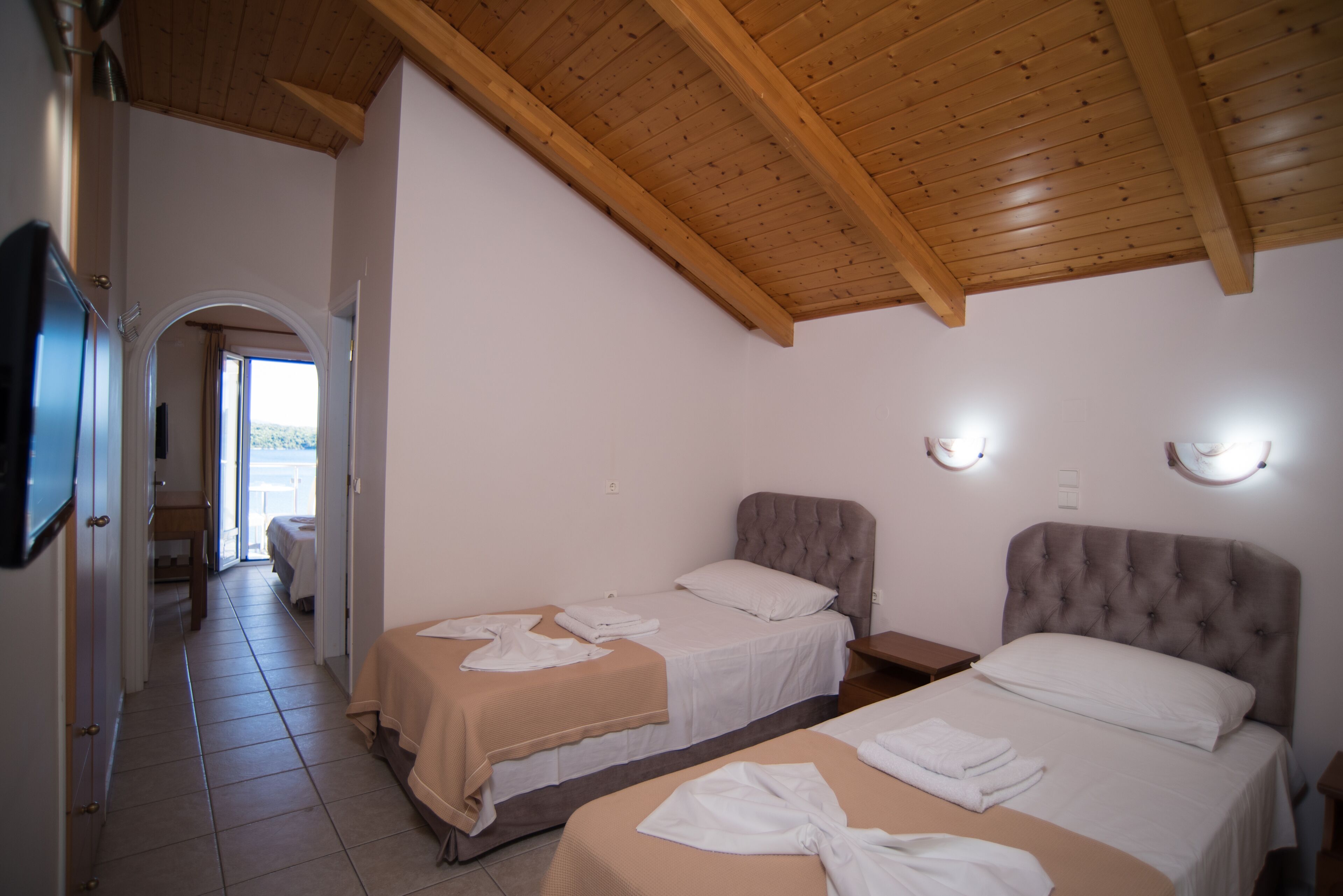 A hotel room with two beds, a wooden ceiling, and a view through an open door.