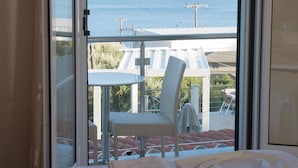 A hotel room with a bed, a view of a lake, and a balcony with a chair and table. - Oasis Hotel (Lefkada)