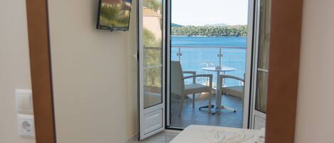 A room with a large mirror reflecting a balcony with a table and chairs, a view of the sea, and a book titled "Agatha Christie" on a wooden surface.