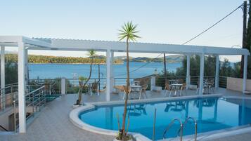 Zona de piscina con vistas al mar, mobiliario exterior y porche cubierto.