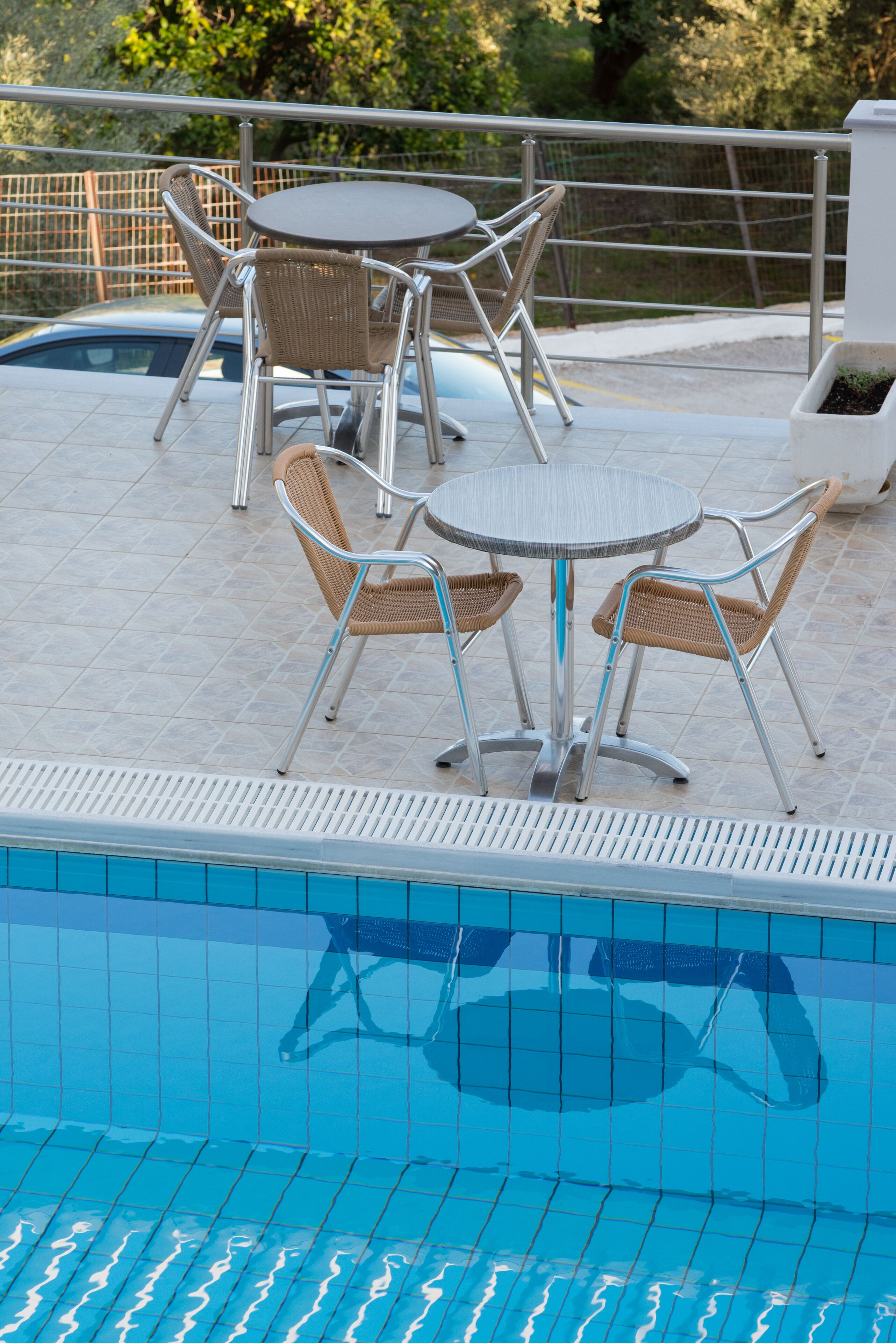 Uma área à beira da piscina com duas mesas redondas e quatro cadeiras de vime.