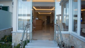 A modern building entrance with glass doors, a stone wall, and a clear view into the interior. - Oasis Hotel (Lefkada)