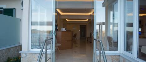 Entrada moderna de un edificio con puertas de cristal, una pared de piedra y vista despejada al interior.