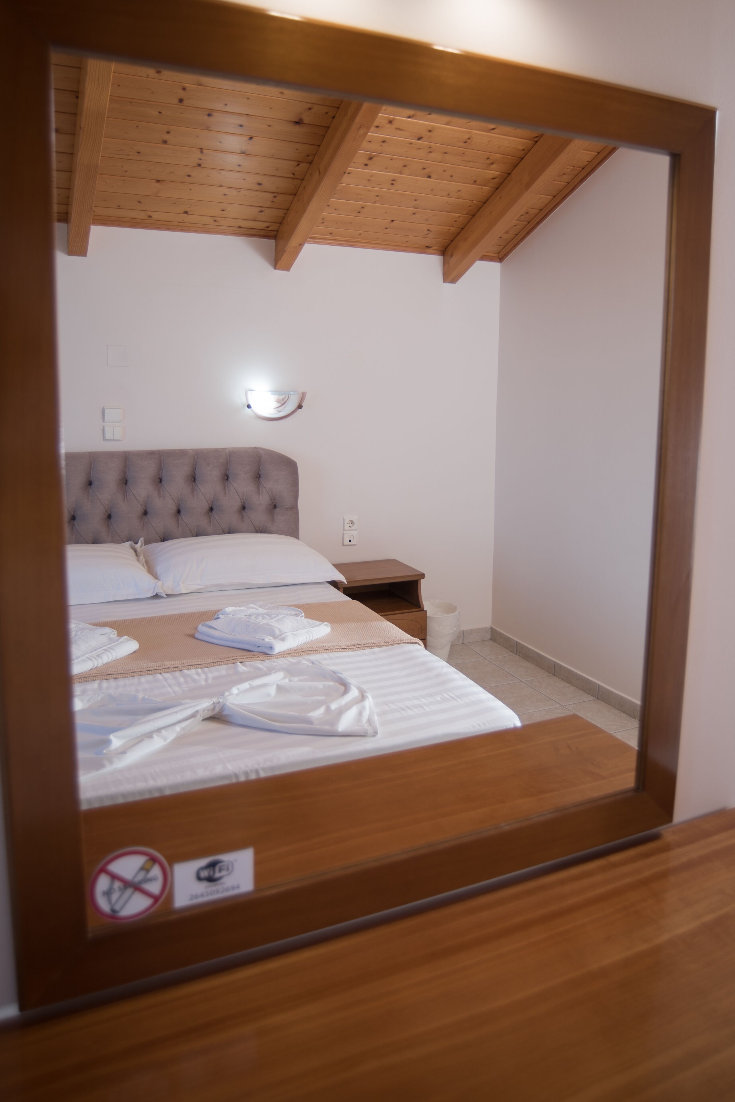 A bedroom with a wooden ceiling, a tufted headboard, a bedside table, and a wall-mounted light fixture.