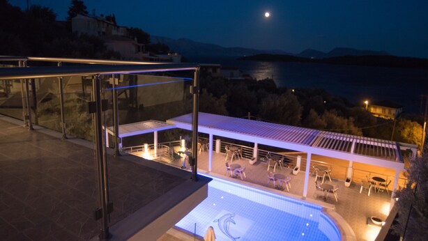 A rooftop pool area with a view of the sea and mountains at night. - Oasis Hotel (Lefkada)