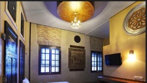 A hotel room with a bed, a chandelier, a television, and decorative wall panels.