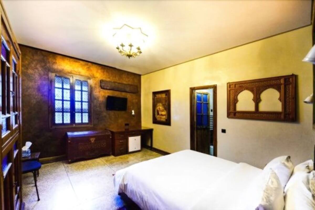 A bedroom with a bed, a dresser, a desk, and a chair. There is a window with a view of the outside.