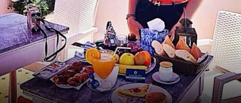 Una mesa de desayuno con pasteles, frutas, una taza de café y una botella de jugo.