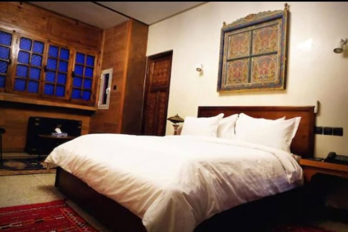 A bedroom with a large bed, wooden walls, a patterned wall hanging, and a red carpet.