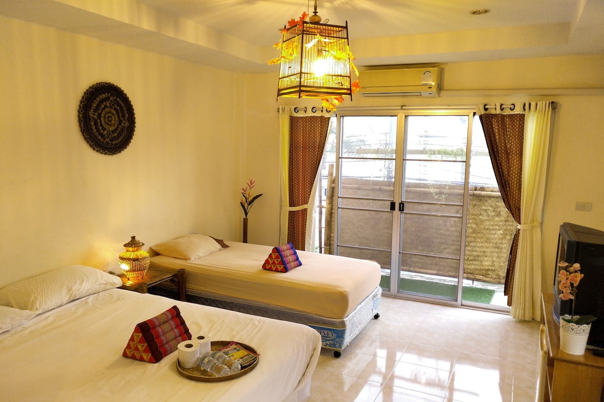 A hotel room with two beds, a small table with toiletries, a TV, and a large window with curtains.
