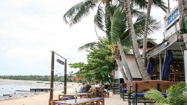 A beachside restaurant with wooden tables and benches, palm trees, and a view of the beach. - Hinkong Hut (Ko Pha-ngan)