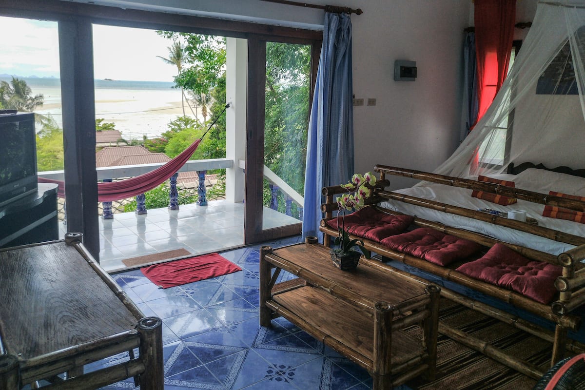 A room with a wooden sofa, a TV, and a view of the sea through a glass door.